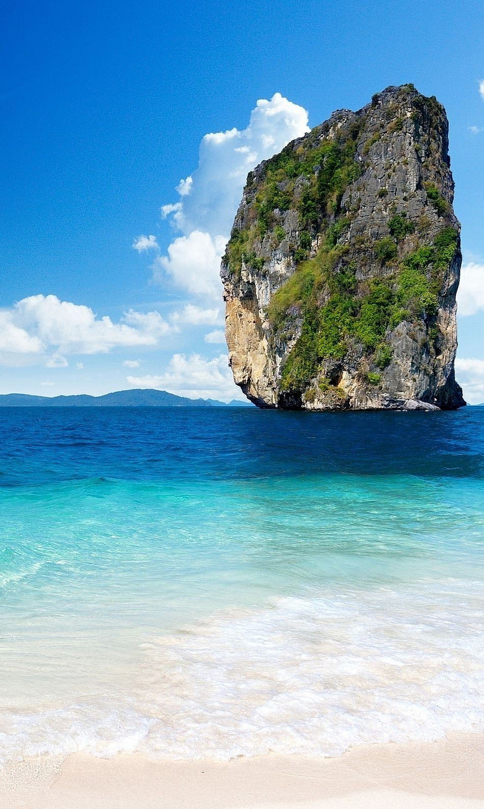 Há uma grande pedra na água perto da praia (verde, colina, areia, mar, árvore)