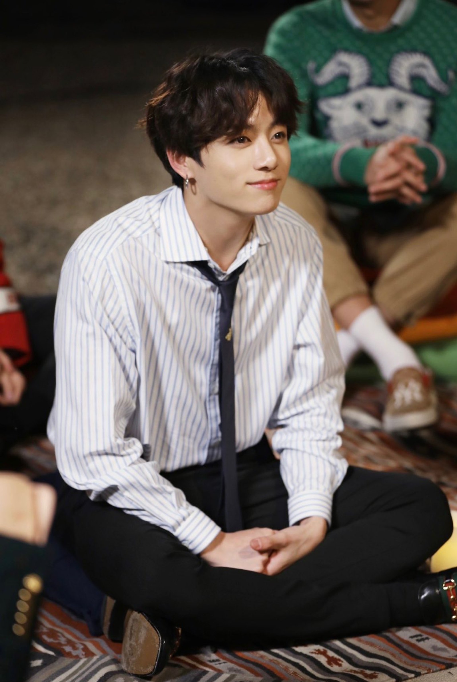 There is a man sitting on the floor with a tie on (army zip, bts, jungkook)