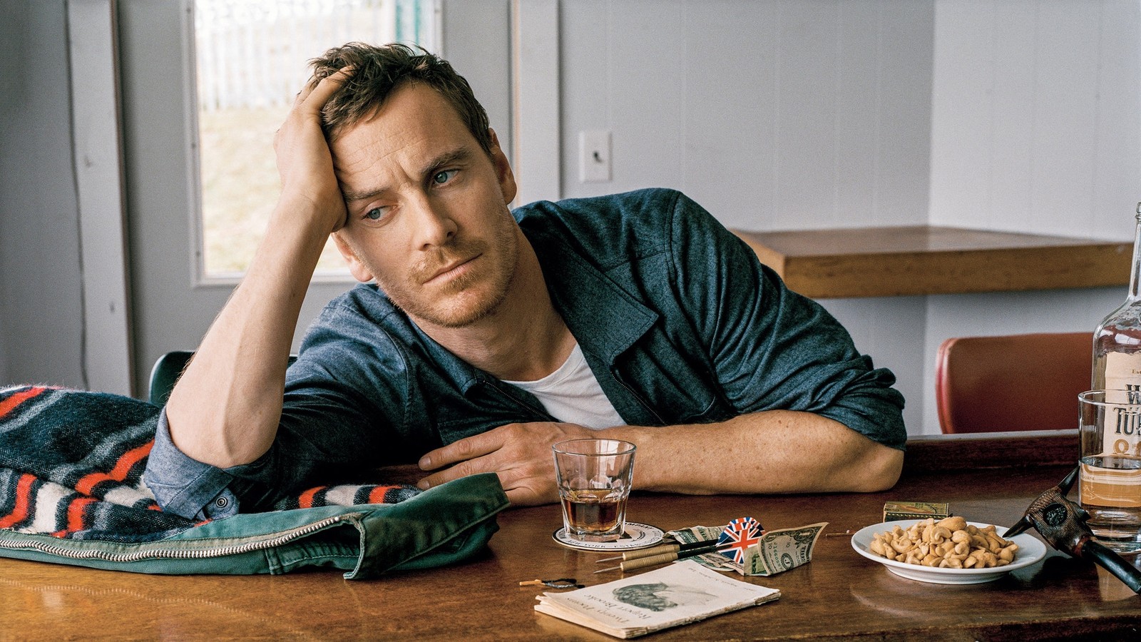 There is a man sitting at a table with a bottle of alcohol (michael fassbender, steve jobs, actor, magneto, new york city)