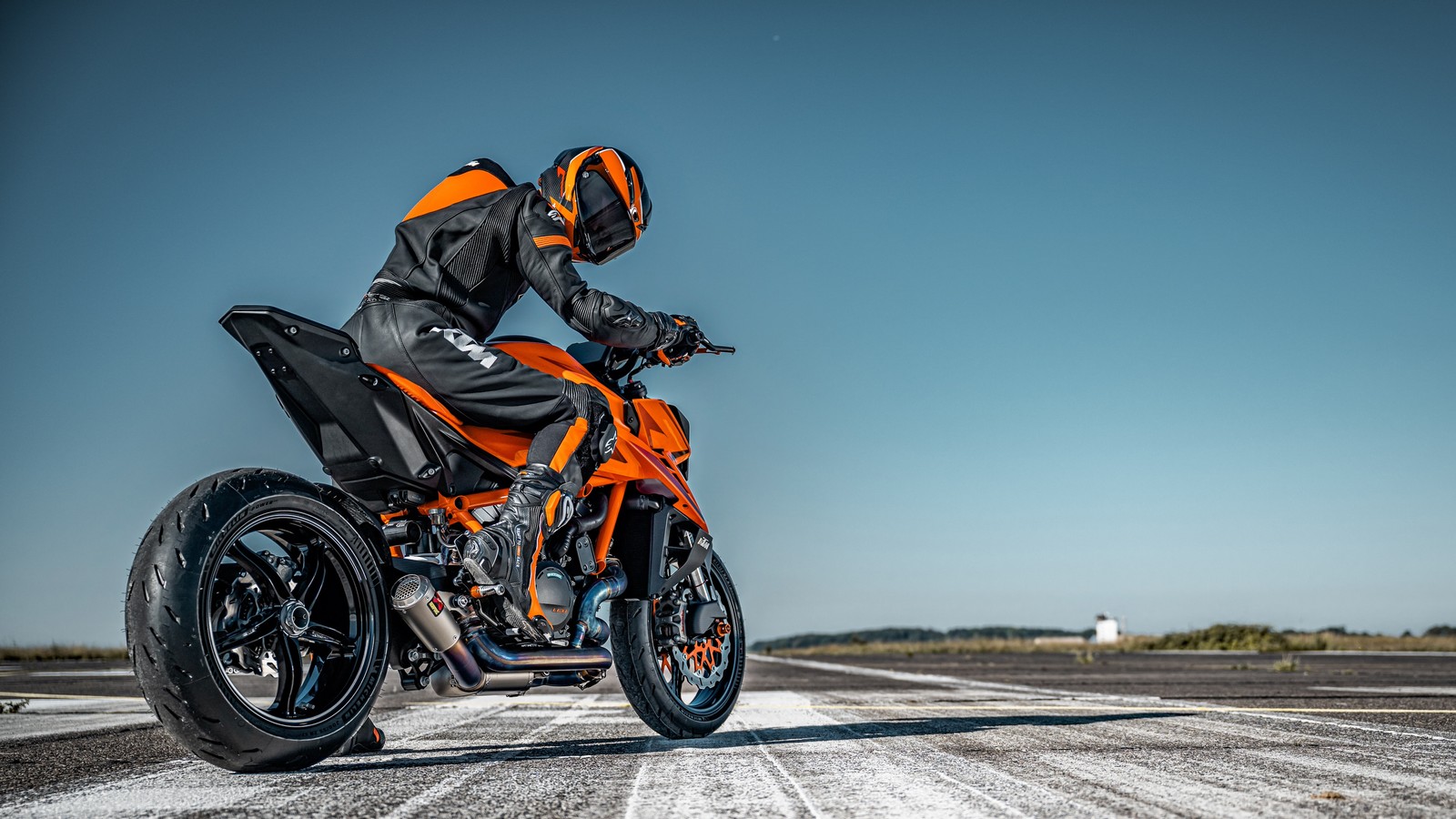 Un hombre con un traje negro y naranja montando una motocicleta en una carretera (ktm 1390 super duke r, motos desnudas, 2024, asfalto, pista de carreras)