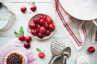 Cerezas frescas y utensilios de repostería dispuestos sobre un fondo pastel, perfectos para una receta de tarta de cereza.