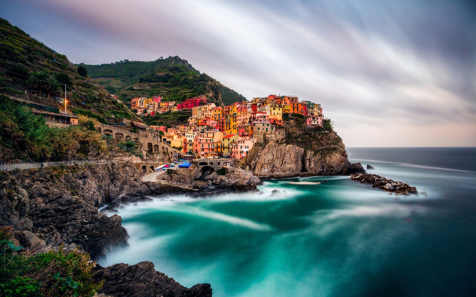 Uma vista de uma pequena cidade na costa com ondas quebrando à sua frente (manarola, costa, corpo de água, natureza, mar)