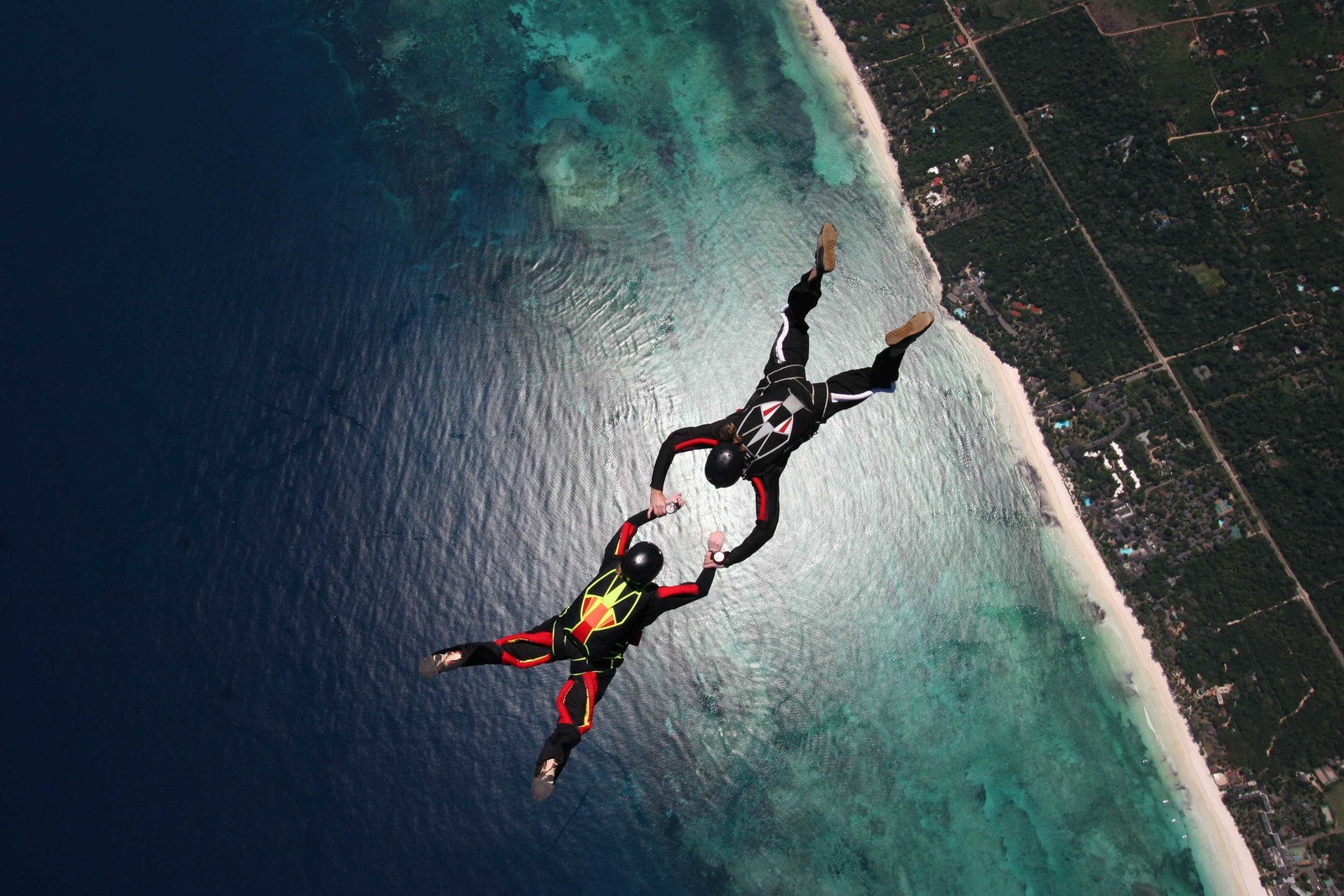 Un homme en costume rouge et noir survole l'océan (parachutisme, sport extrême, aventure, recréation, sports)