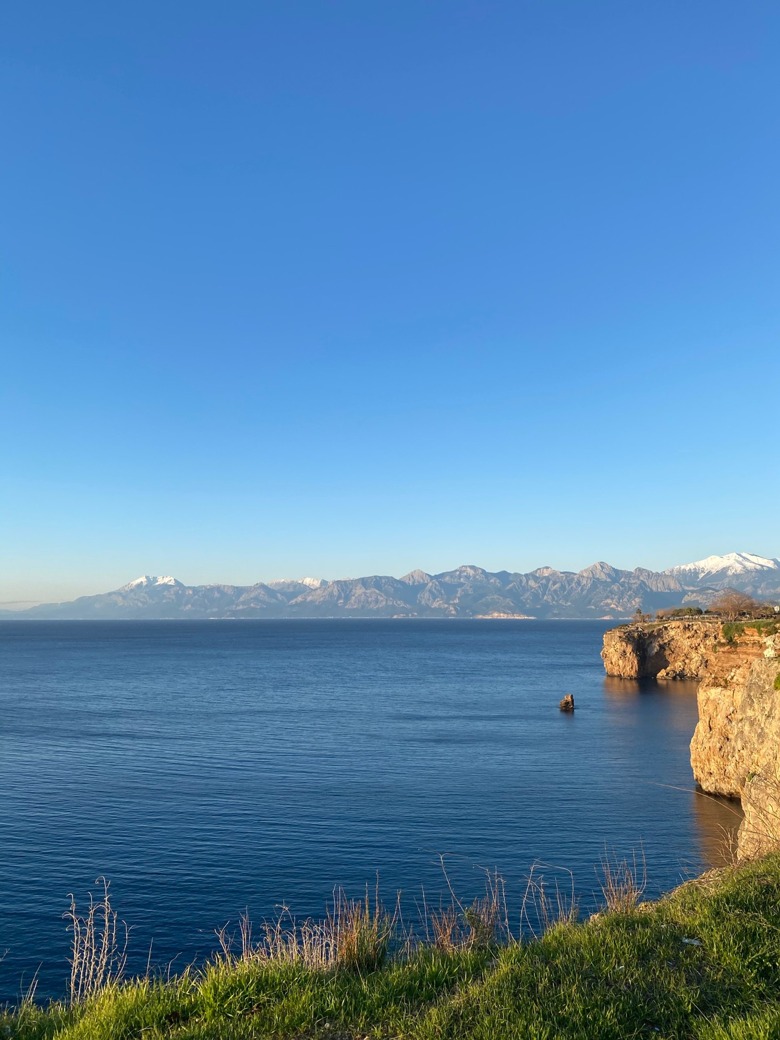 Un homme musclé sur une falaise surplombant l'océan et les montagnes (langue, eau, plante, nuage, montagne)