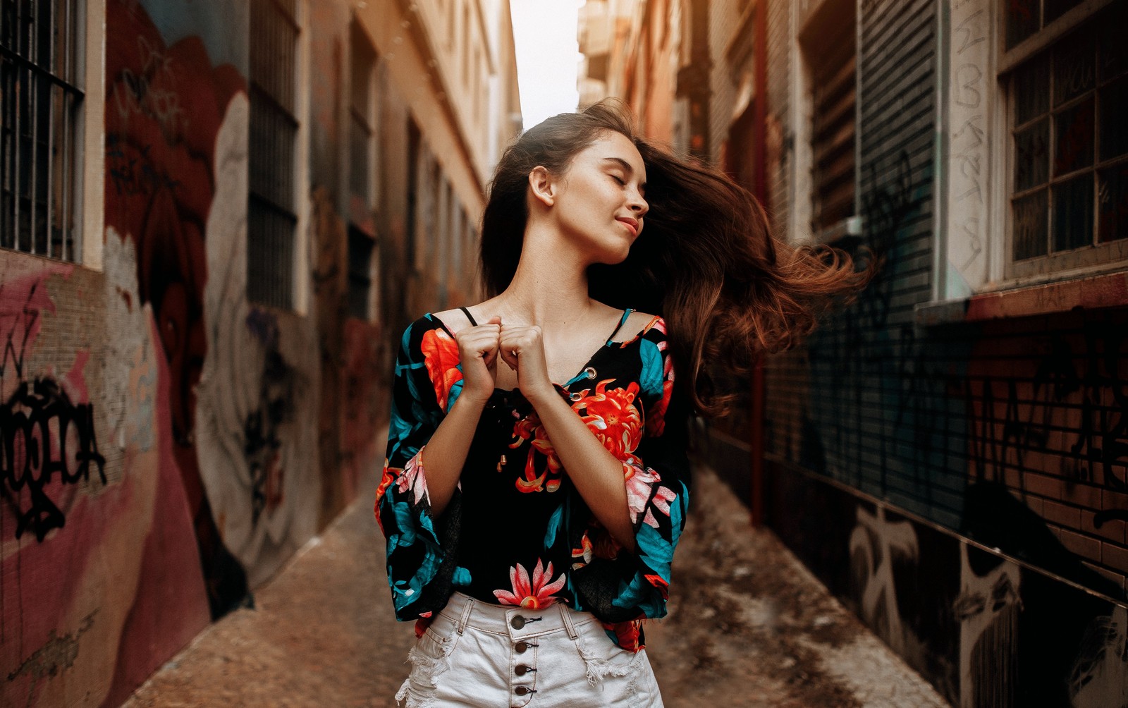 Una mujer con cabello largo está de pie en un callejón con una blusa colorida (hombro, moda callejera, ropa, belleza, moda)