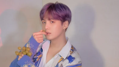 Suga de BTS con cabello morado, atuendo elegante y una pose juguetona con uvas.