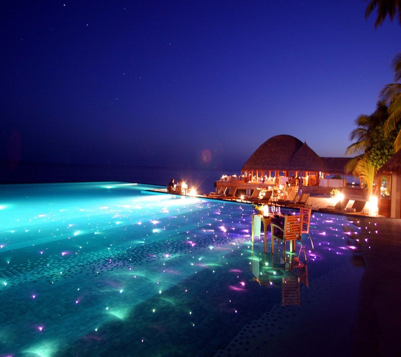 Nighttime view of a pool with lounge chairs and a thatched hut (2160x1920, wallpaper)