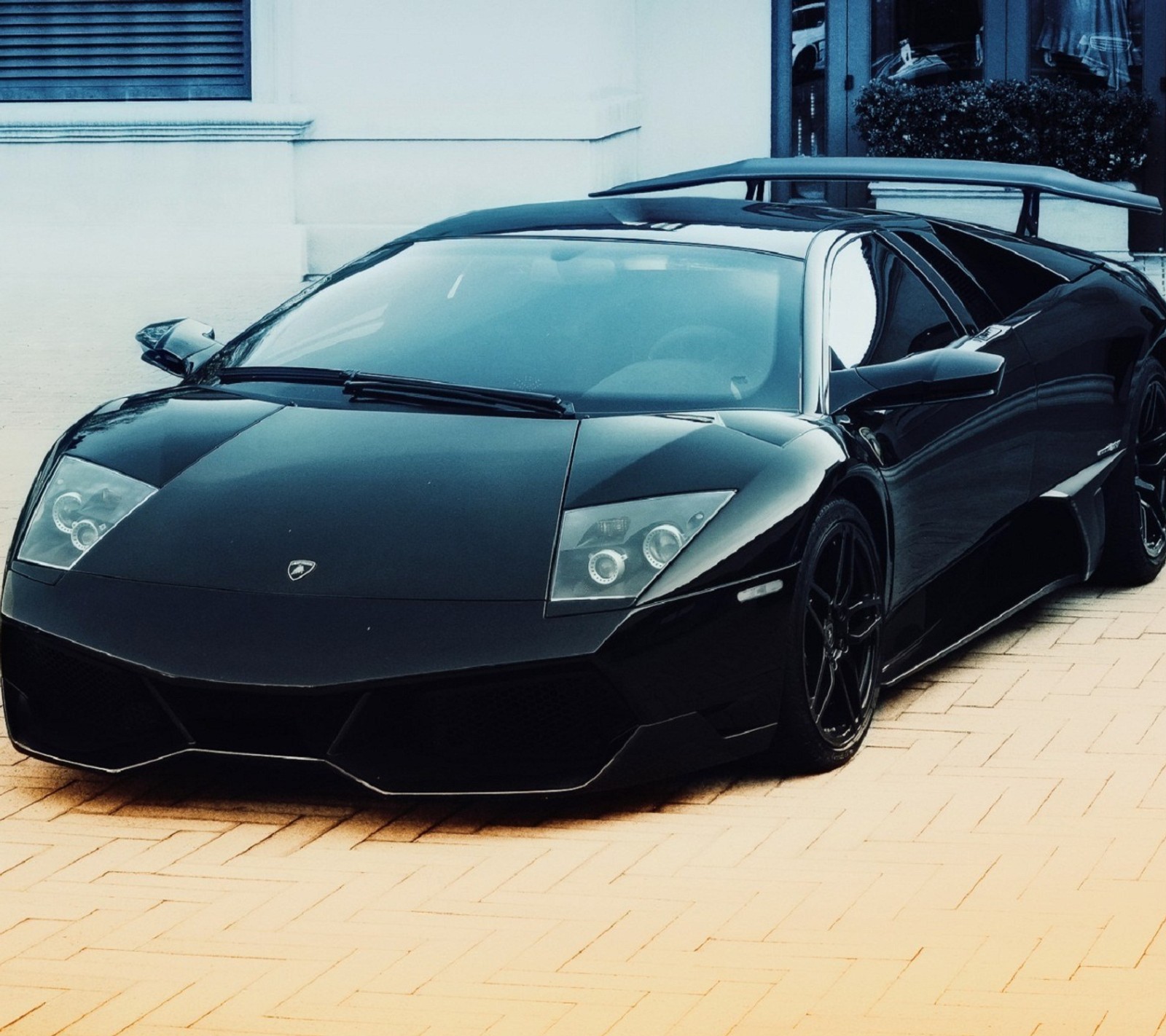 A close up of a black sports car parked on a brick road (bentley, dodge, ferrari, lamborghini, mustang)