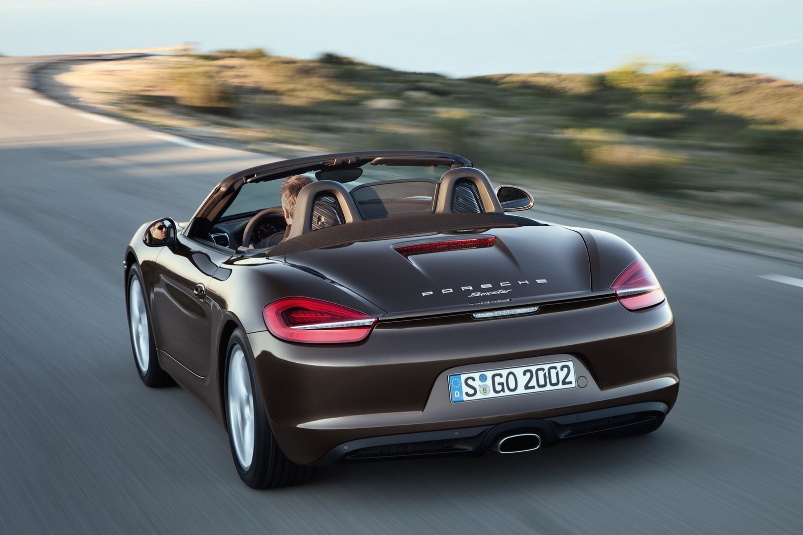 Un porsche roadster marrón conduciendo por una carretera con una montaña al fondo (2012 porsche boxster, porsche boxster 2014, 2014 porsche boxster, porsche boxster 2015, 2015 porsche boxster)