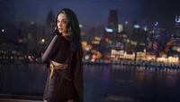 Emma Dumont in a stylish outfit against a vibrant city skyline at night.