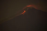 Volcán escudo en erupción por la noche con flujo de lava y nubes de ceniza sobre la Ciudad de Guatemala