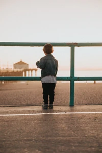 Child Gazing at the Ocean Horizon from the Beachside Fence