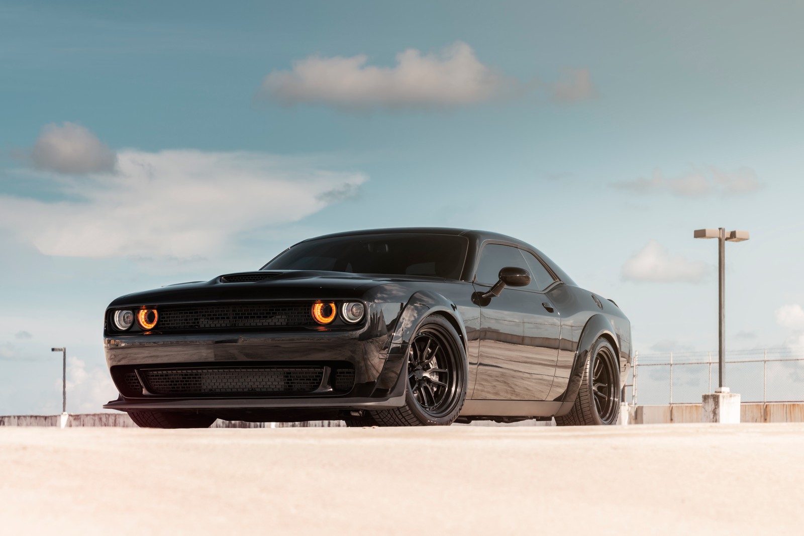 Une dodge challenger noire garée sur un parking sous un ciel nuageux (jeep, chevrolet camaro, voiture, dodge, muscle car)