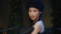 Sana de TWICE dans une pose élégante, portant un chapeau noir chic et une ambiance rêveuse avec un éclairage doux et un feuillage décoratif.