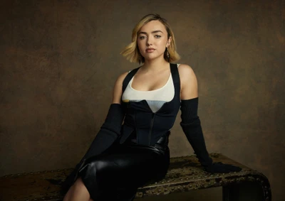 Peyton List em um traje preto estiloso, sentada com confiança contra um fundo texturizado.