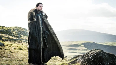 Jon Nieve con una capa de piel, de pie en un paisaje rocoso con un cielo dramático de fondo.