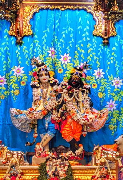 A vibrant altar featuring intricately adorned deities of Krishna and Radha, surrounded by floral decorations and traditional offerings.