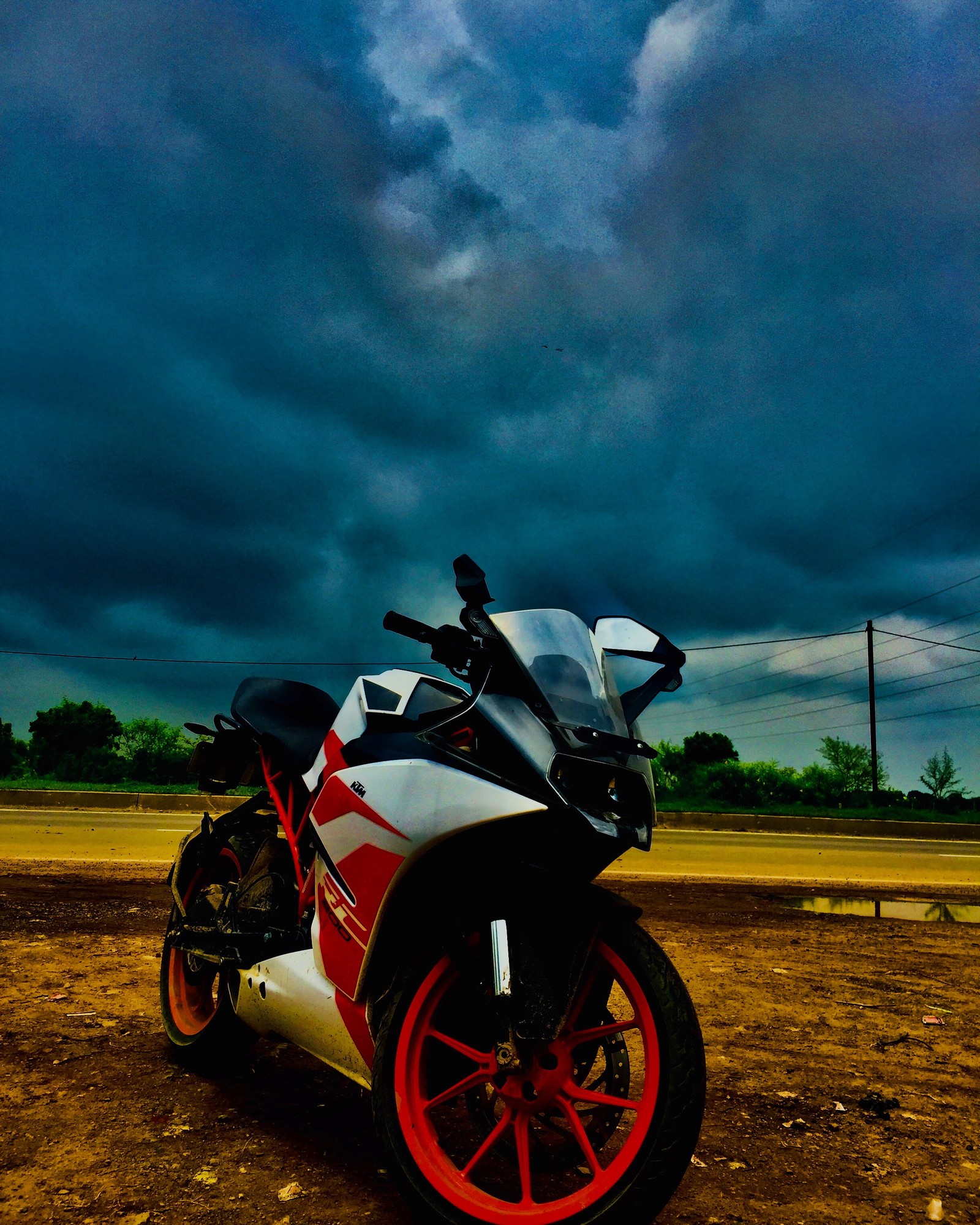 Verschwommenes bild eines motorrads, das auf einer schotterstraße unter einem bewölkten himmel geparkt ist (ktm, rc200)