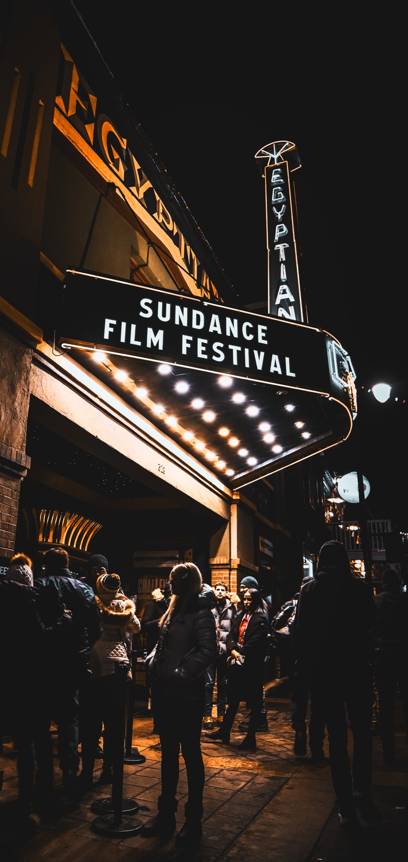 Люди, стоящие перед театром ночью с вывеской, на которой написано sundance (струнный инструмент, концерт, электричество, город, автомобильное освещение)