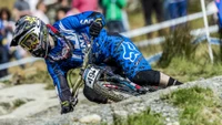 Ciclista de montaña en acción, compitiendo cuesta abajo en un sendero rocoso, mostrando habilidades de deportes extremos mientras usa equipo de protección y un casco.