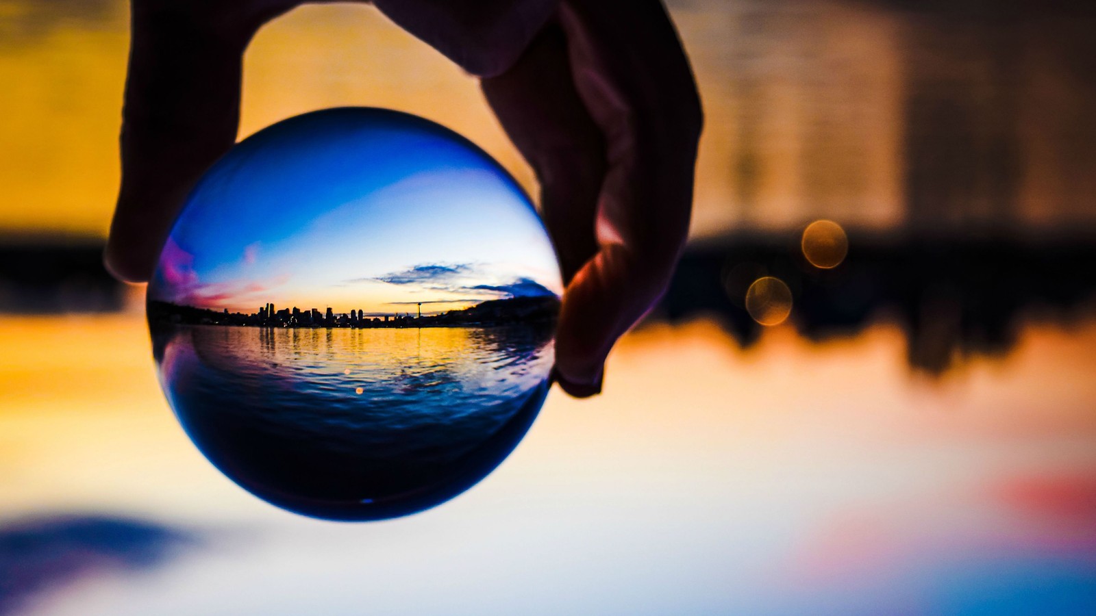 Someone holding a crystal ball with a sunset in the background (reflection, water, blue, ball, light)