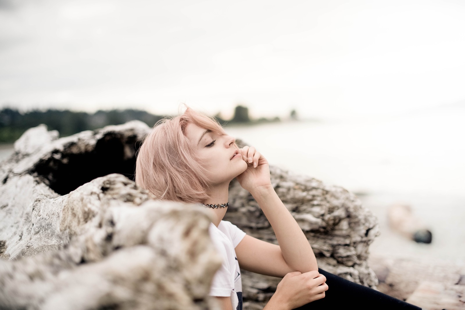 Blond woman sitting on rocks by the water with her eyes closed (people in nature, beauty, skin, eye, sitting)