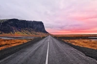 Estrada aberta serena levando a um penhasco majestoso sob um céu rosa na Islândia