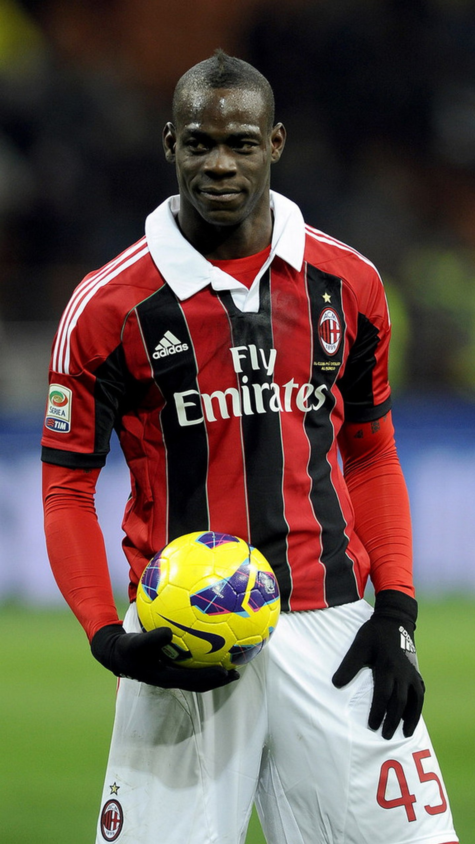 Un hombre árabe con uniforme rojo y negro sosteniendo un balón de fútbol (mario balotelli, milán, milan)