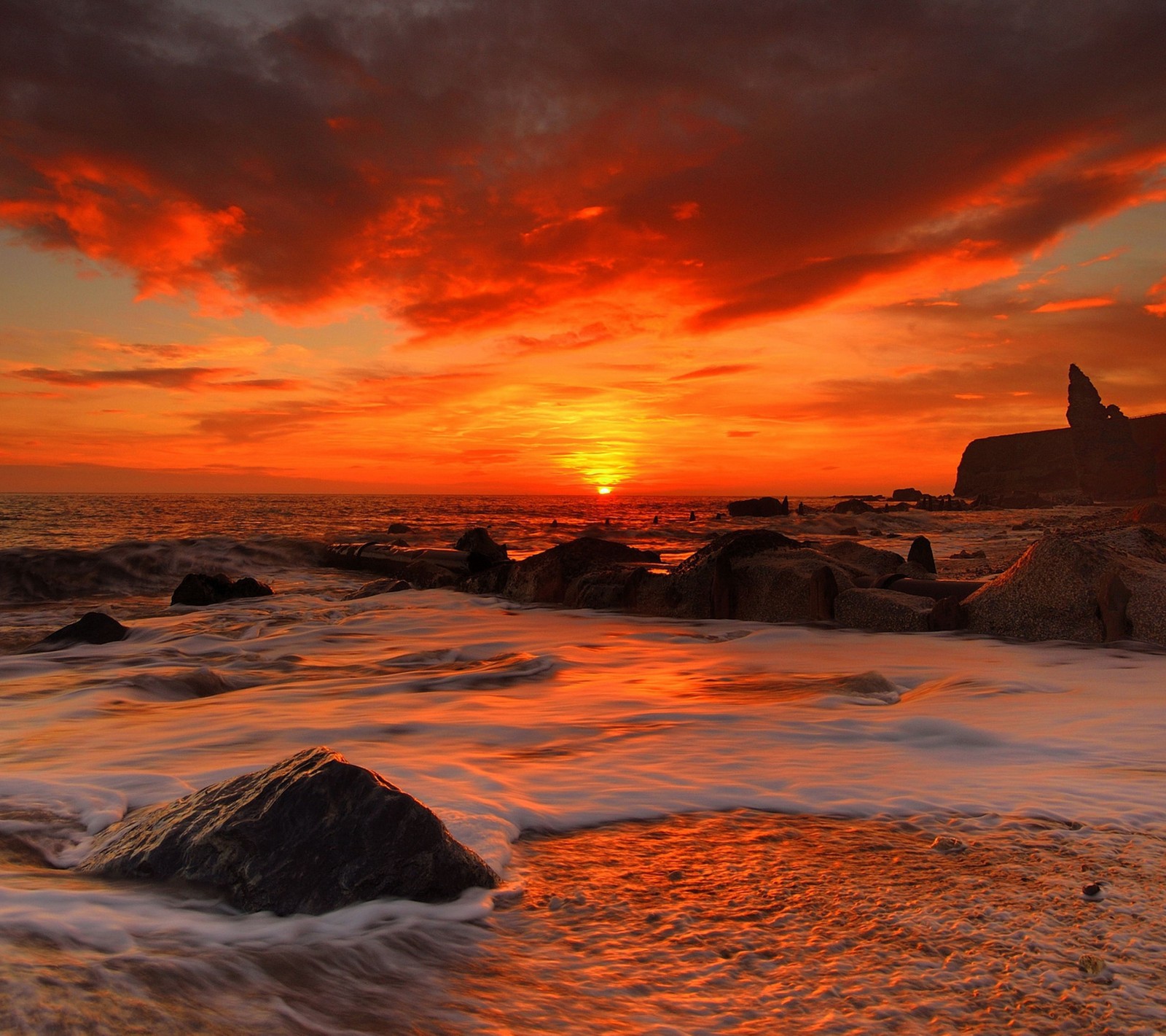 Sunset over the ocean with rocks and waves in the foreground (cloud, orange, red, rock, sea)