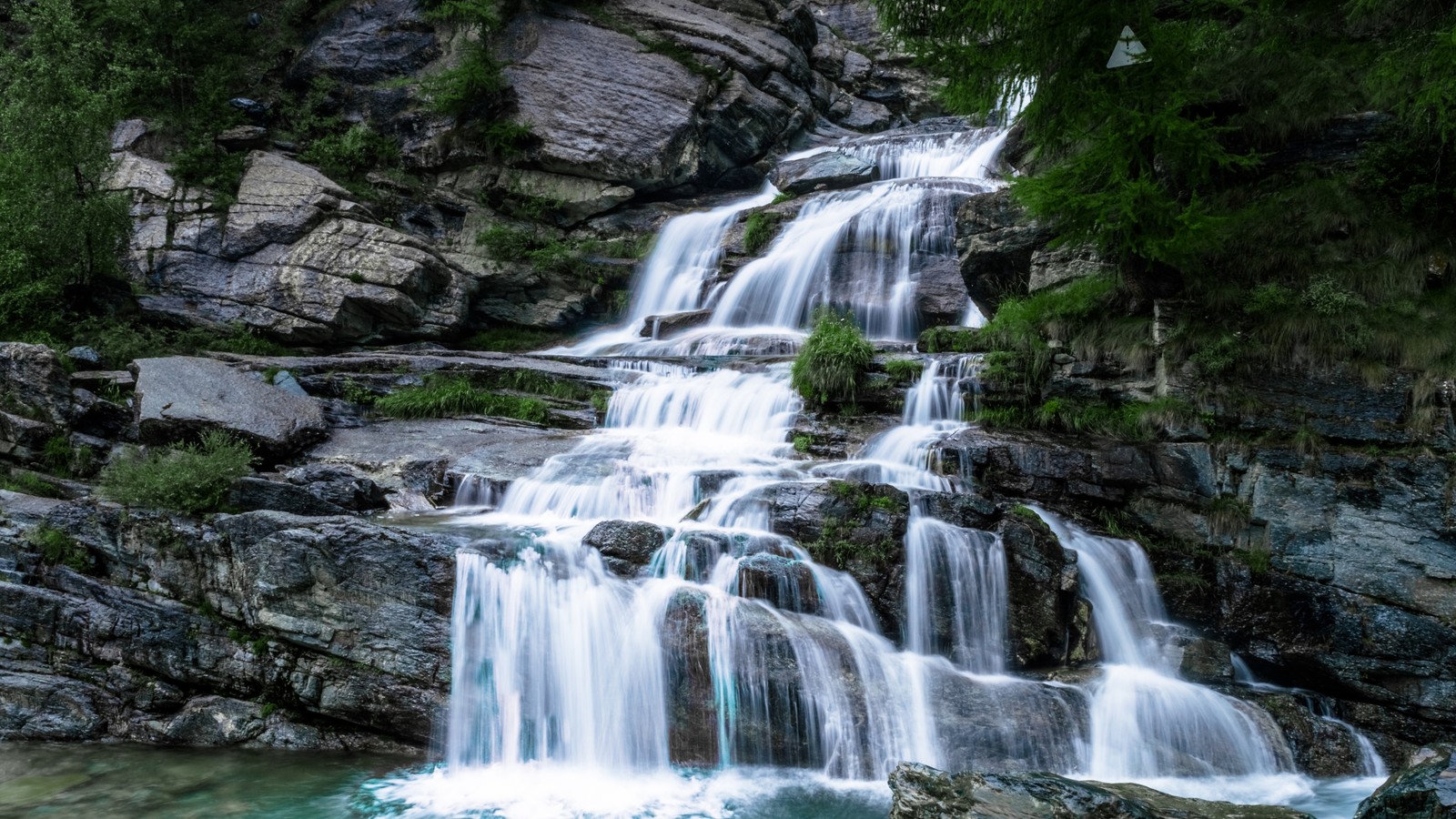 Um close de uma cachoeira com uma pessoa em pé em uma pedra (cachoeira, curso dágua, água, planta, natureza)