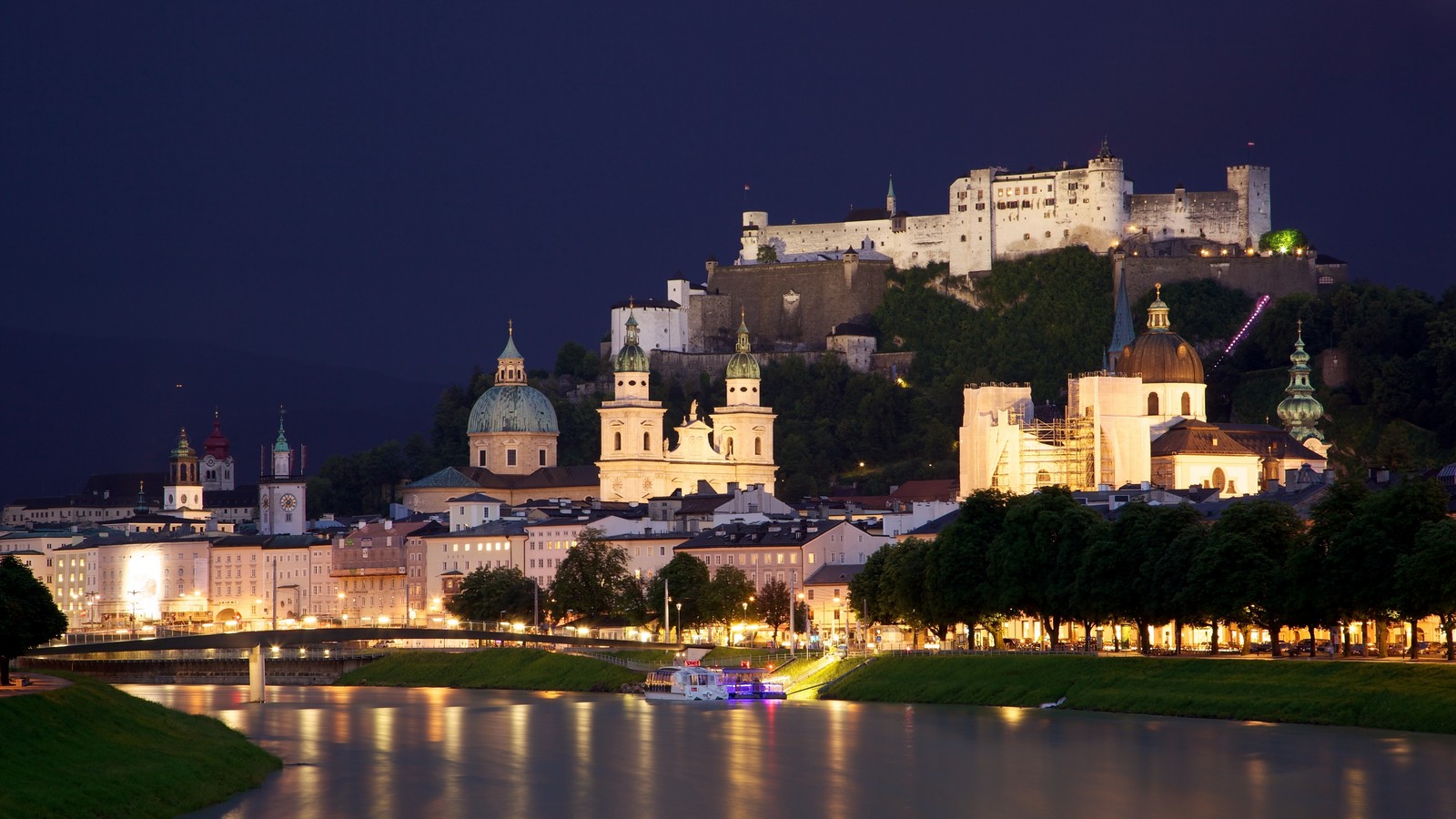 Uma vista aérea de uma cidade com um castelo em uma colina ao fundo (salzburgo, salzburg, viena, noite, marco)