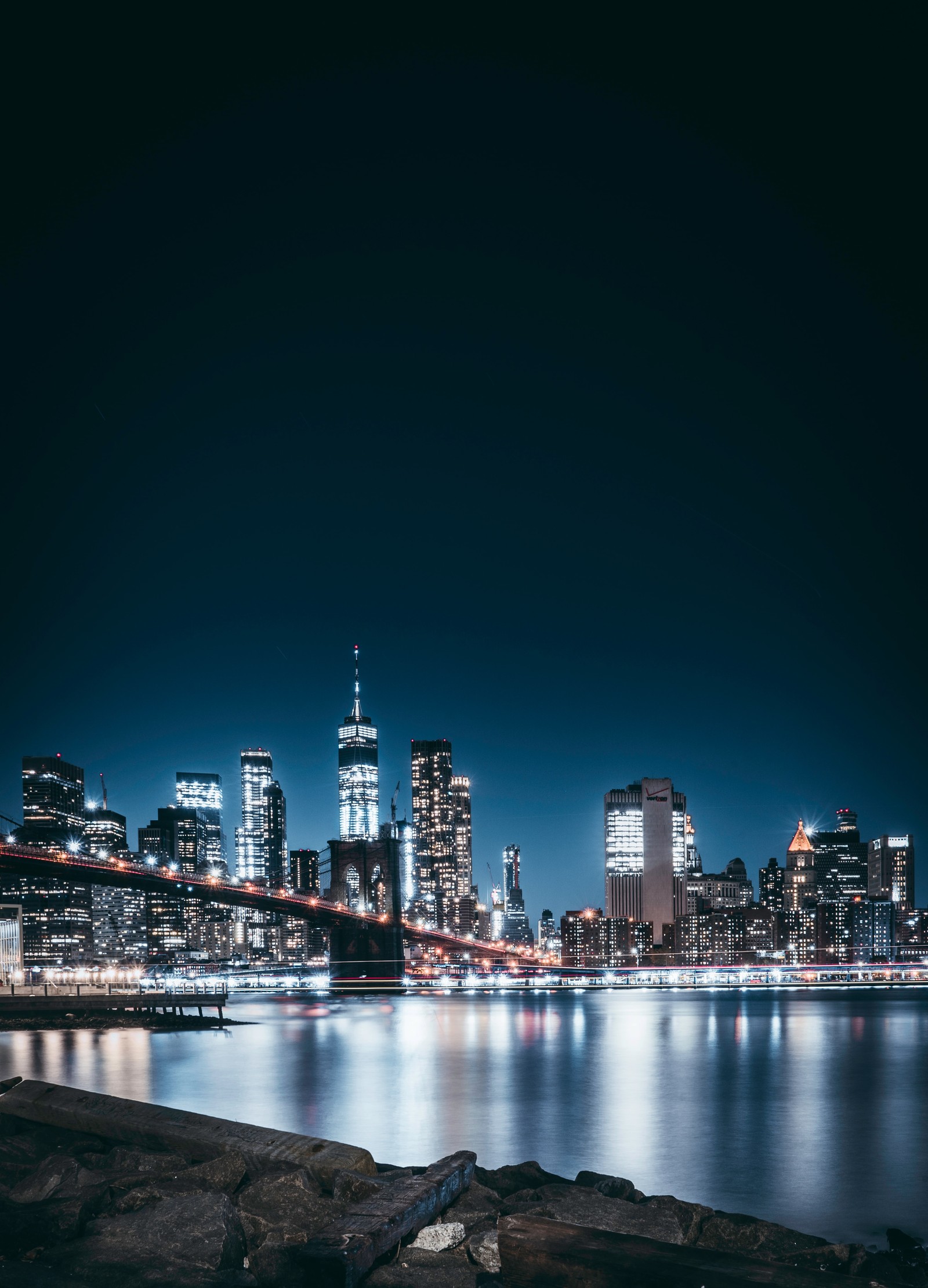 A view of a city skyline at night with a bridge (brooklyn bridge, city lights, night, cityscape, reflections)