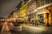 Scène vibrante du soir d'une rue charmante à Copenhague, avec des façades colorées, des repas en plein air et une atmosphère animée.