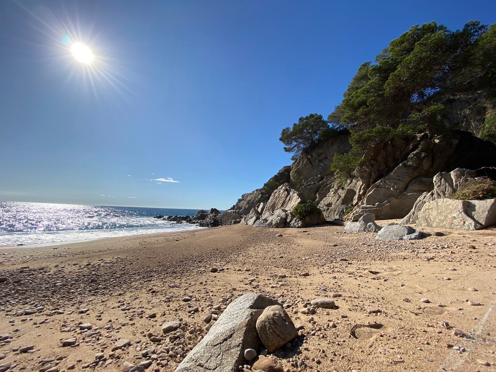 Há uma grande rocha na praia perto da água. (mar, costa, areia, rocha, sol)