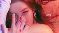 Sunmi em um close vibrante, exibindo uma maquiagem marcante e arte de unhas intrincada contra um fundo colorido.