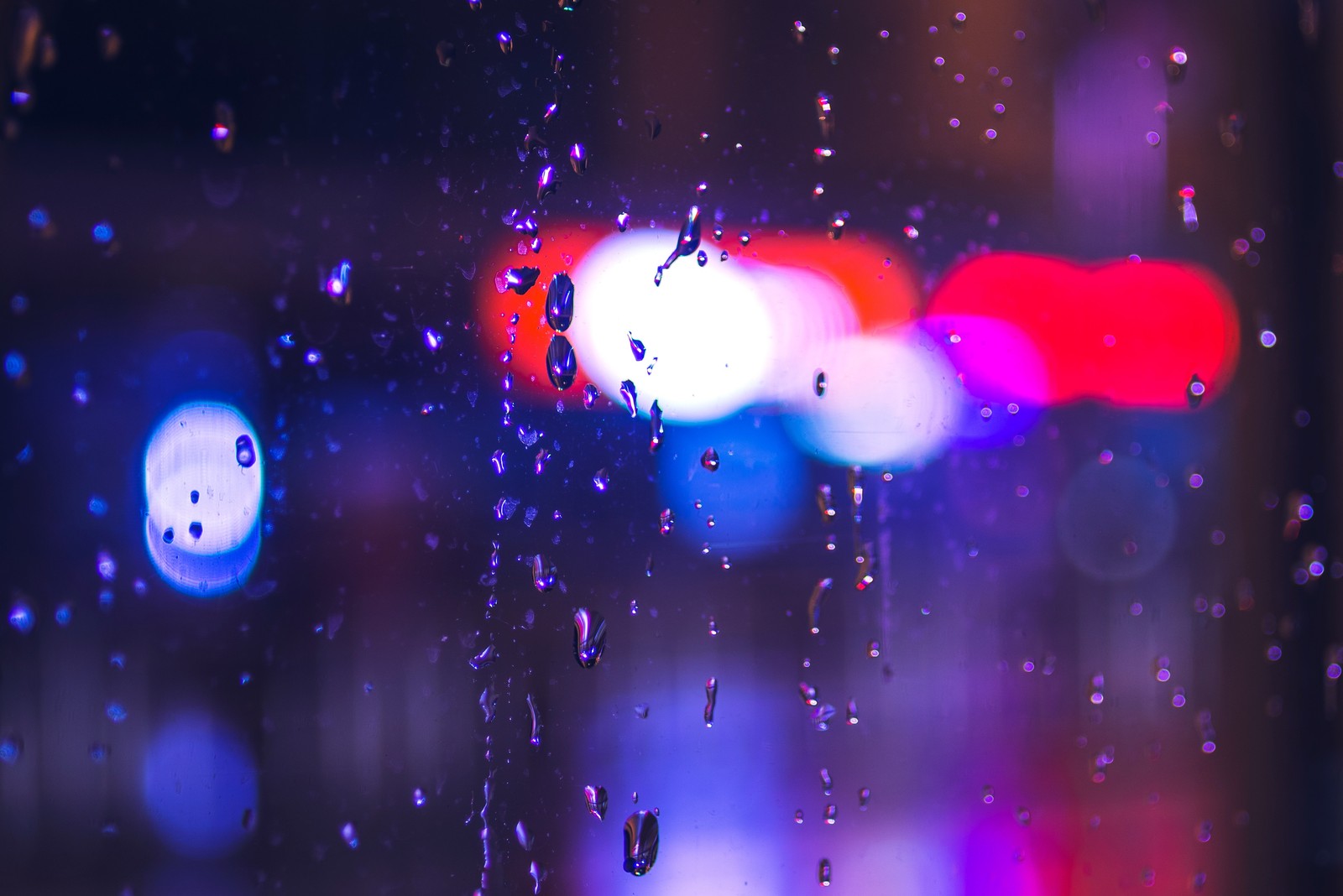 A close up of a rain covered window with a blurry background (bokeh, light, purple, violet, water)