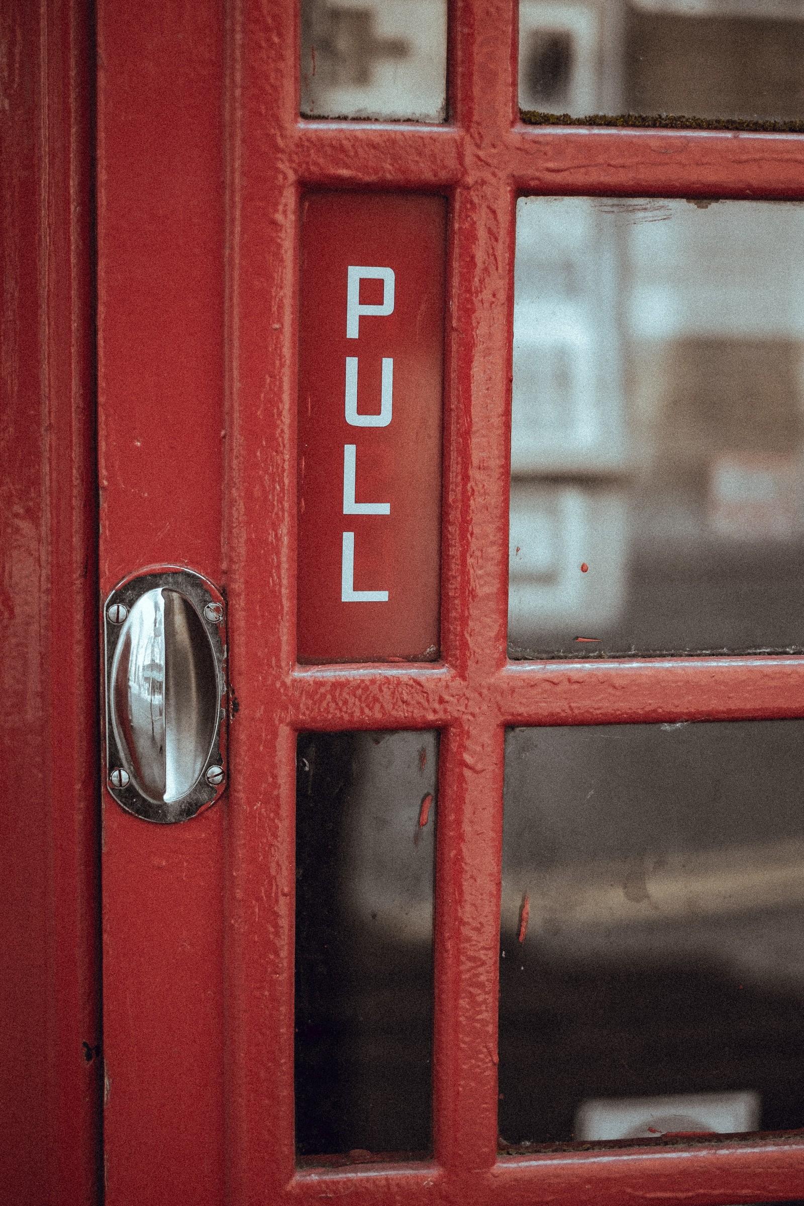 There is a red phone booth with a sign on it (window, door, wall, red, number)