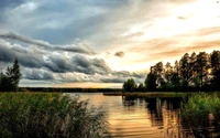 Nature sereine au coucher du soleil : lac réfléchissant entouré de rives luxuriantes et de nuages dramatiques