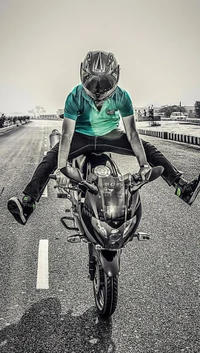 A daring stunt rider performing a split on a motorcycle on an open road.