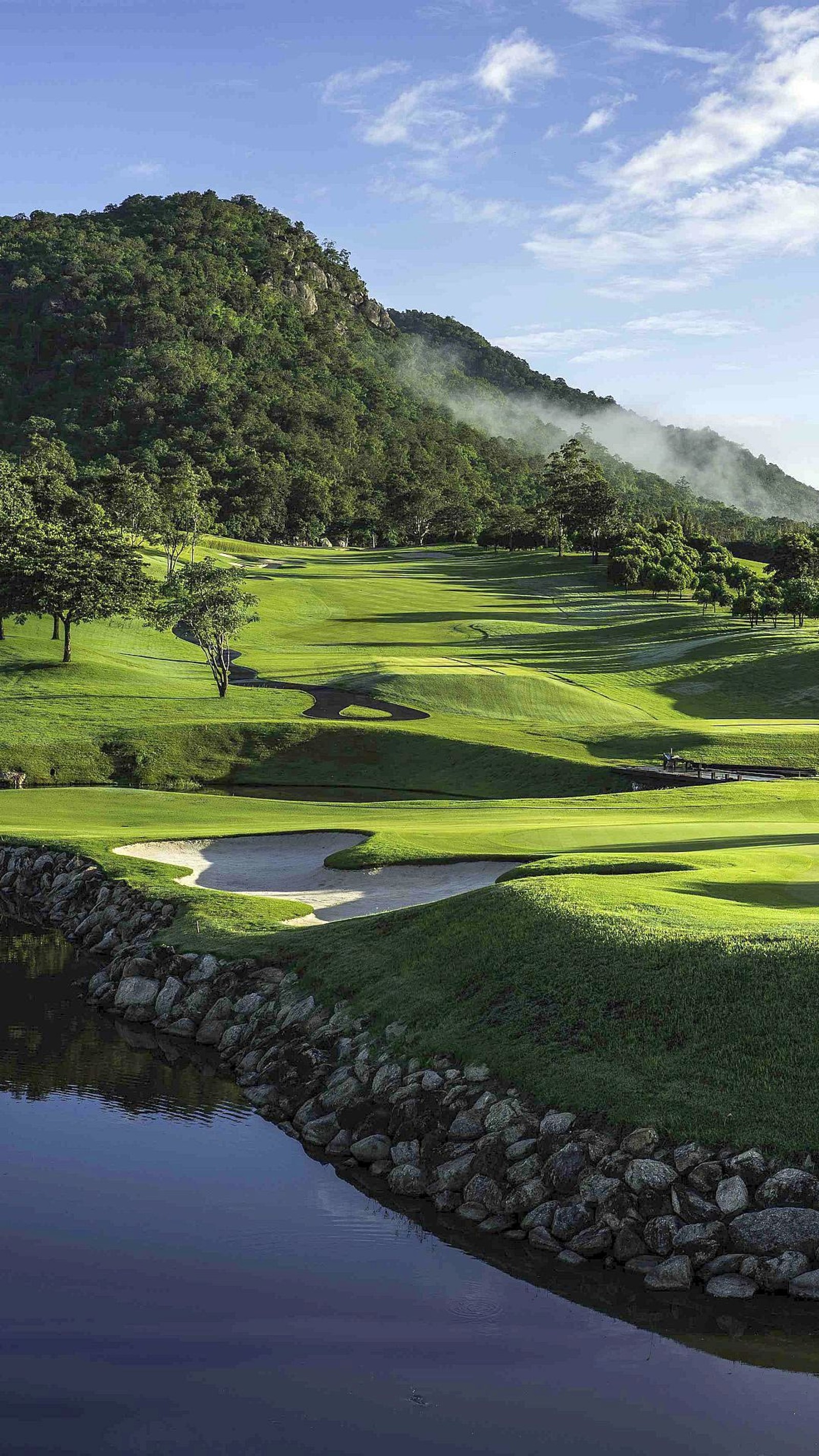 Arafed view of a golf course with a pond and a mountain in the background (balls, clubs, course, golf, greens)