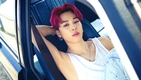 Jimin from BTS lounging effortlessly in a car, showcasing his iconic red hair and stylish casual wear.