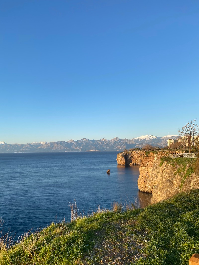 Скамейка стоит на краю скалы с видом на воду (водные ресурсы, вода, лазурный, гора, растение)