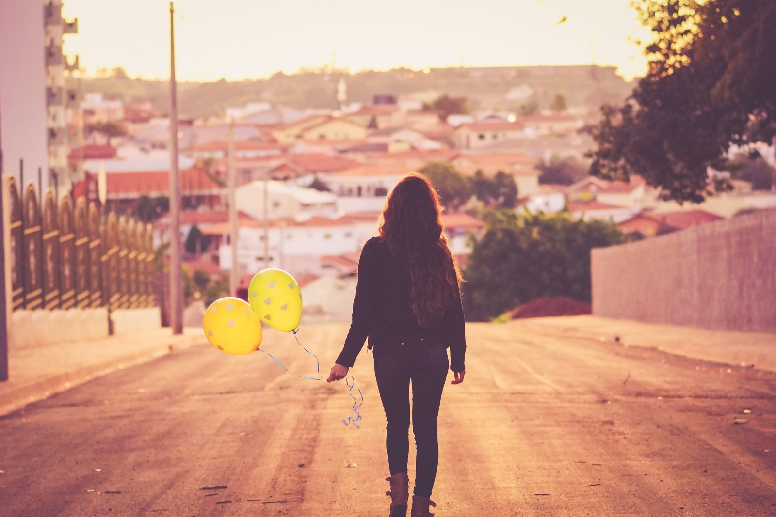 Uma mulher árabe caminhando pela rua com balões na mão (amarelo, luz, beleza, retroiluminação, luz solar)