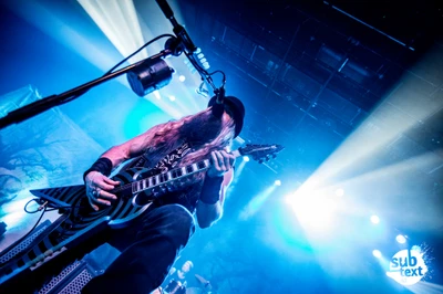 Dynamic rock performance featuring a guitarist passionately playing a strikingly designed electric guitar on stage, illuminated by vibrant stage lights.