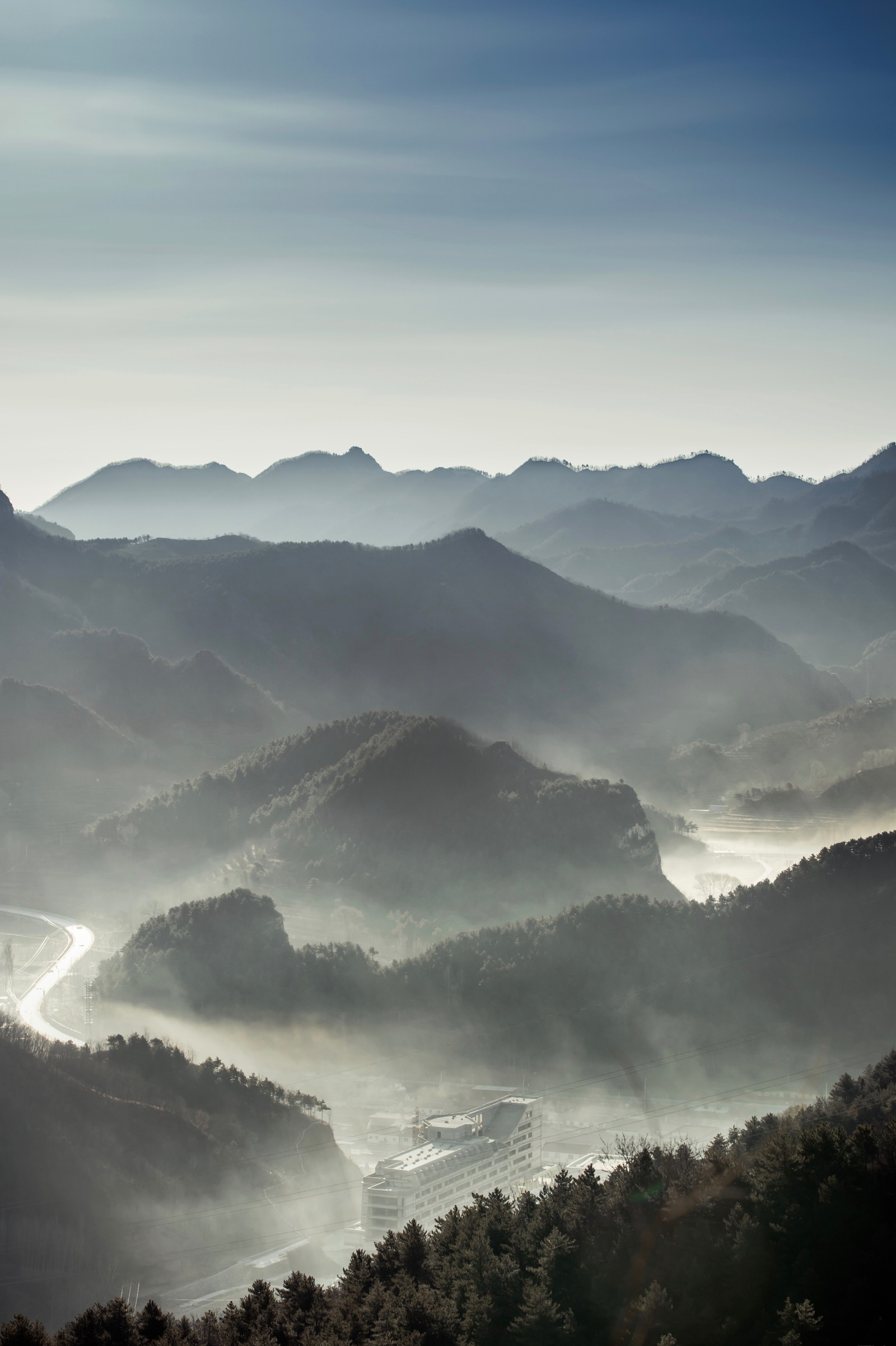 Berge, die mit nebel und dunst bedeckt sind, mit einem fluss, der durch sie fließt (gebirgskette, berg, alpen, hochland, gebirgige landformen)