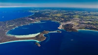 Vista aérea de un paisaje costero que presenta un archipiélago, una península y un puerto, mostrando el vibrante mar azul, las exuberantes formaciones terrestres verdes y las intrincadas formaciones costeras cerca de Perth.