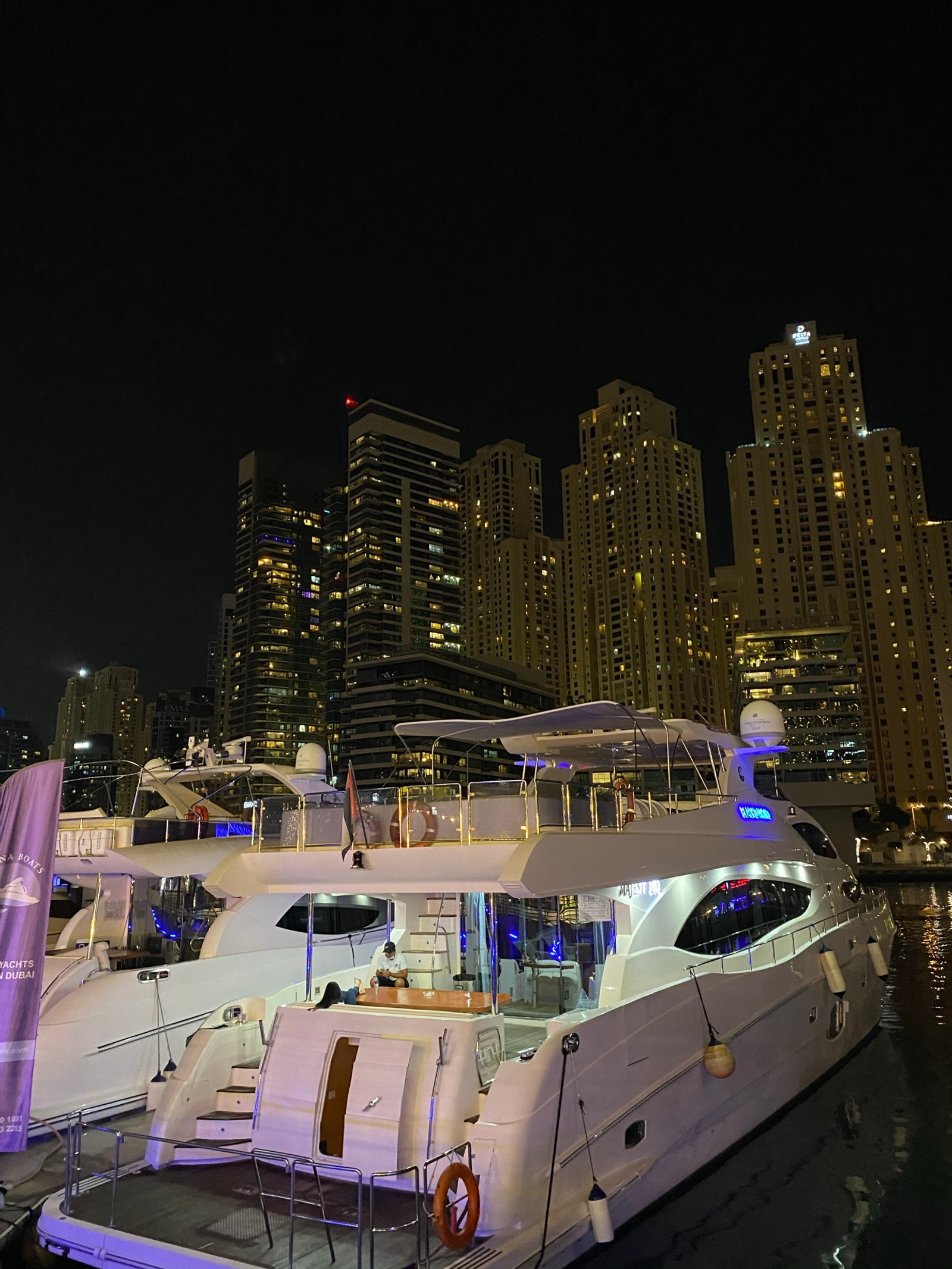 Barcos atracados en un puerto por la noche con luces de la ciudad al fondo (noche, ciudad, embarcación, metrópolis, rascacielos)