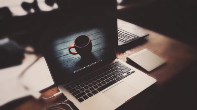 MacBook em uma mesa com uma caneca e um bloco de notas