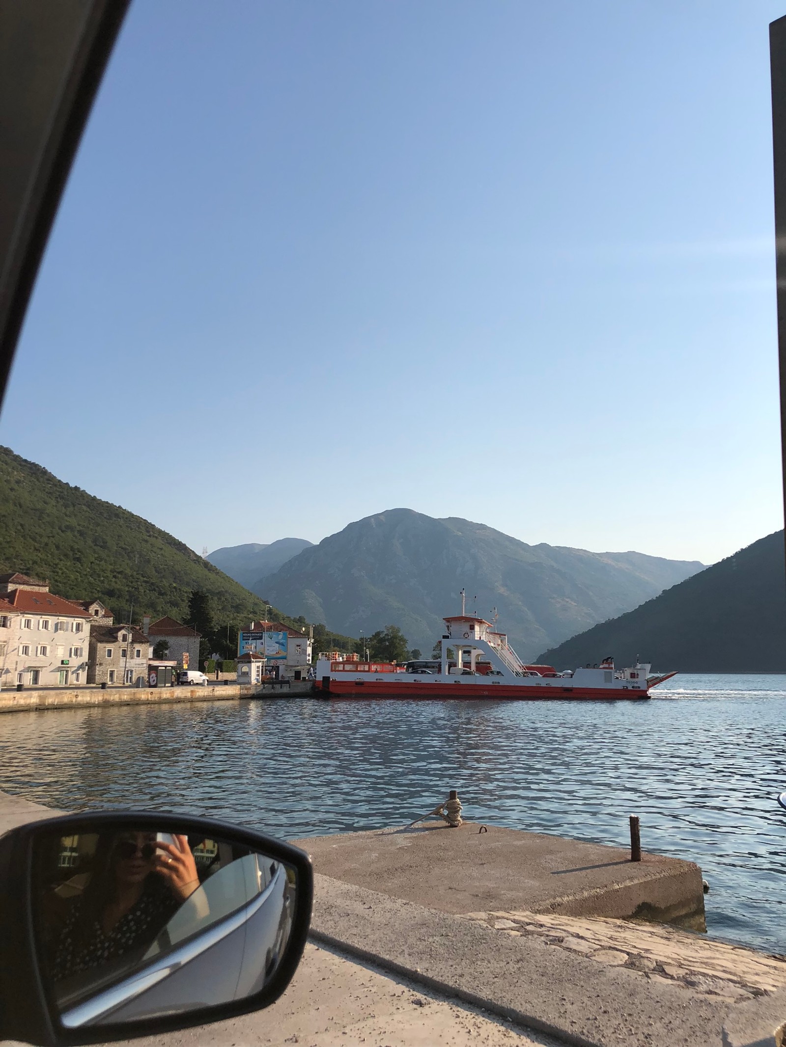 Vue aérienne d'un bateau dans l'eau près d'un quai où une personne prend une photo (eau, bateau, fjord, formes montagneuses, miroir automobile)