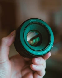 Close-up of a Canon 50mm f/1.8 STM camera lens held in a hand, showcasing its green detailing and clear glass.